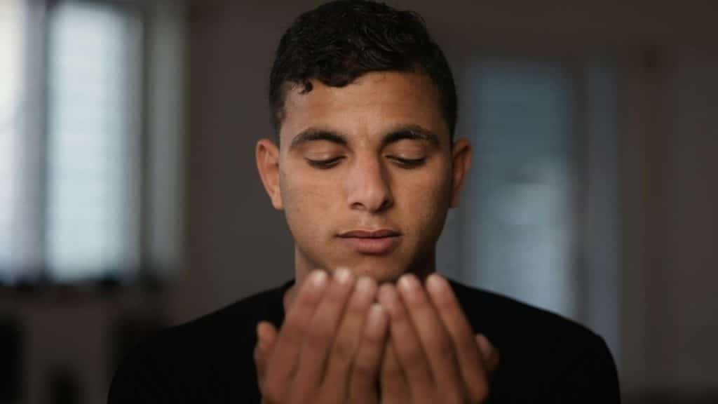 A man with closed eyes holds cupped hands in front of his face.