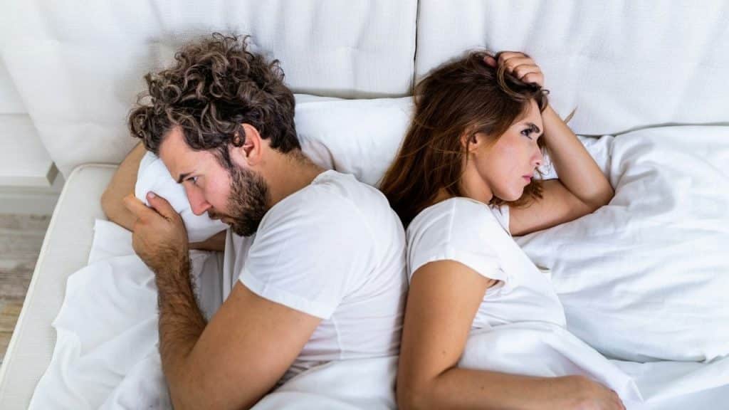 An overhead view of a couple in bed, turning their backs to each other.