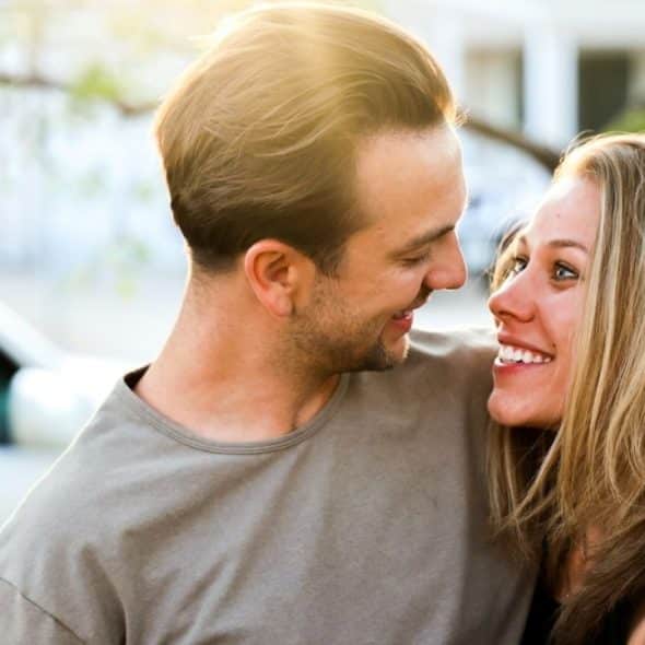 Happy couple embracing and smiling at each other outdoors with a car in the background.