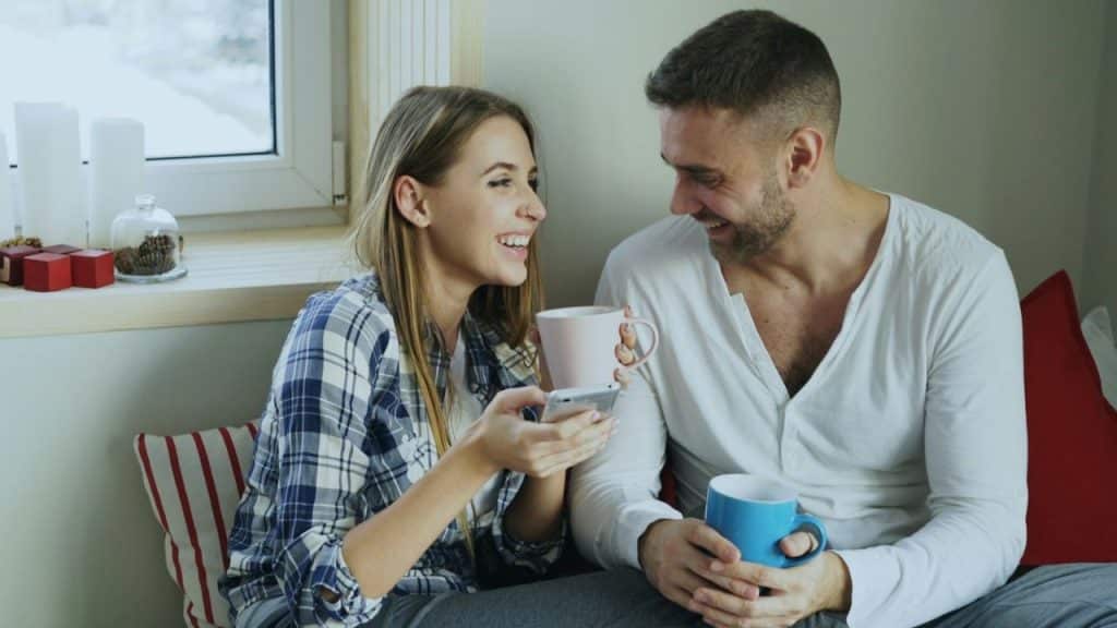 Happy couple sitting by a window, drinking coffee, and looking at each other.
