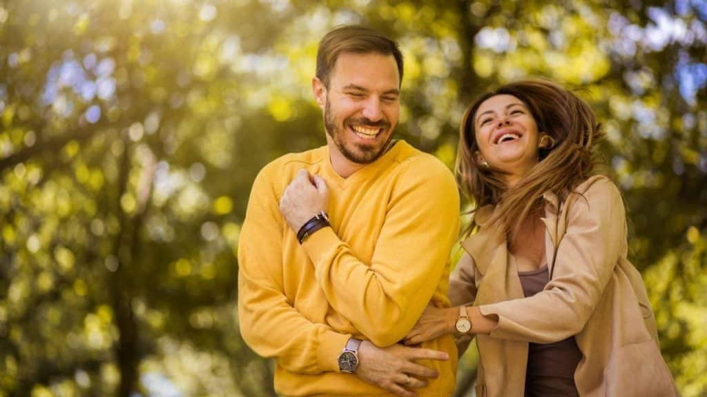 Happy couple laughing outdoors with a bright, sunlit, green and yellow background.