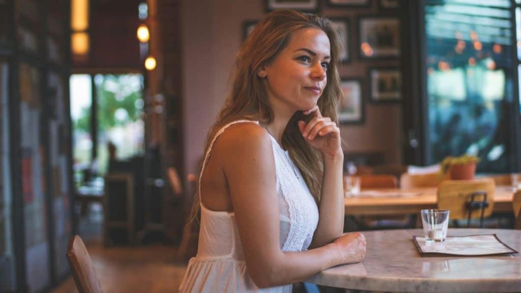 Woman in a white top sitting at a marble table in a cafe, looking thoughtfully away.