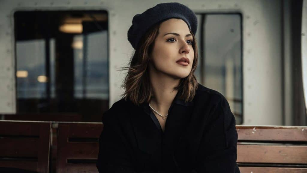 Woman wearing a dark beret and a pearl necklace, sitting and looking off into the distance.