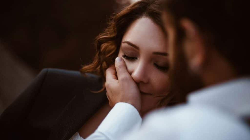 A woman with closed eyes is being gently touched on the cheek by a man's hand.