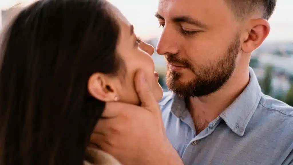 A bearded man holding a woman’s face and smiling.