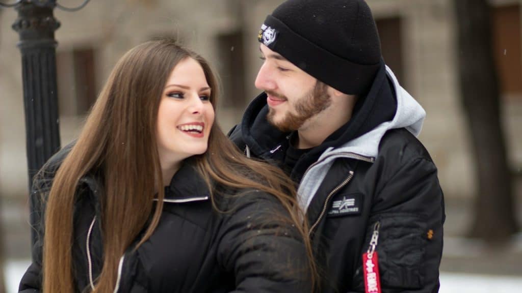 A bearded man in winter clothing is holding a smiling woman tightly.