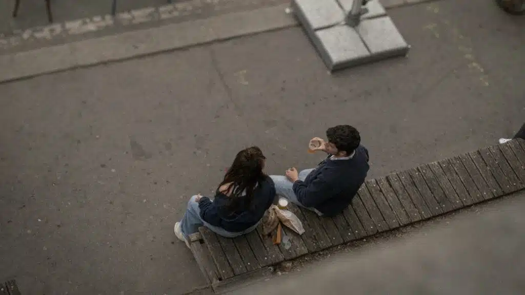A man talking to a woman while they sit on a bench on the street.