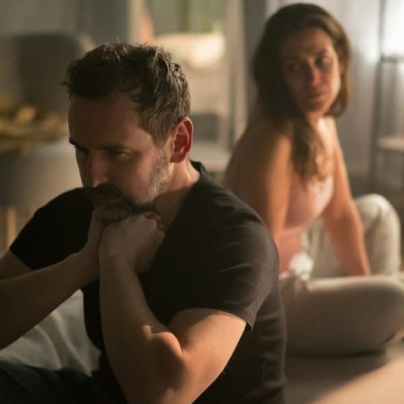 An upset mature man with his wife in bed behind him.