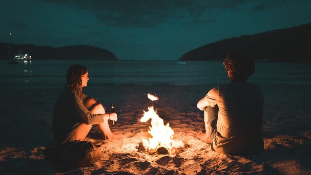 A couple sitting near a fire by the beach at night.