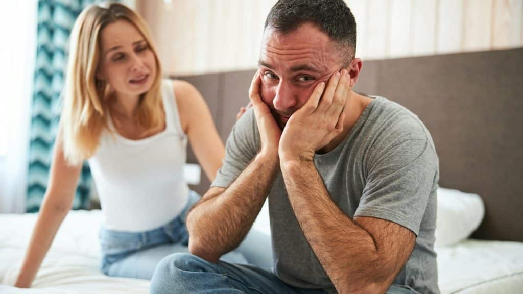 A man holding his face with his hands and looking at the camera while a woman touches his shoulder.