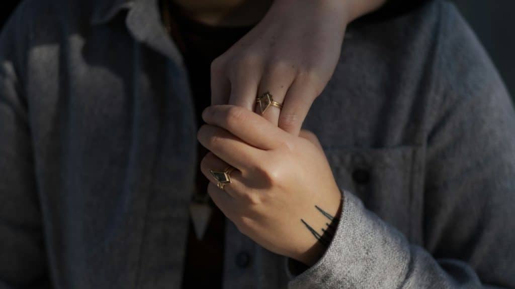 A close-up of two hands gently clasped together, both wearing matching gold geometric rings.