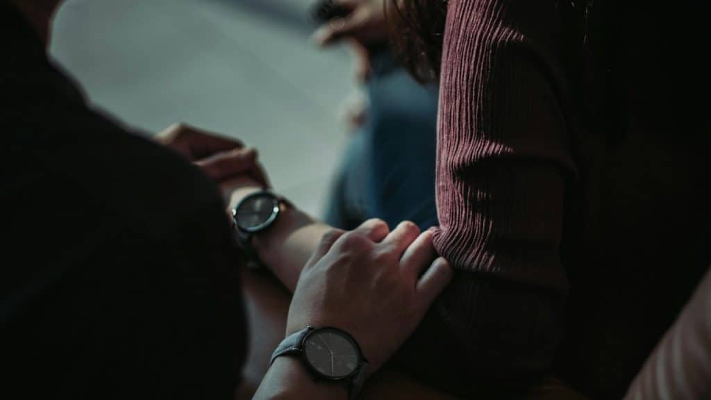 A close-up of two people holding hands, both wearing identical wristwatches.