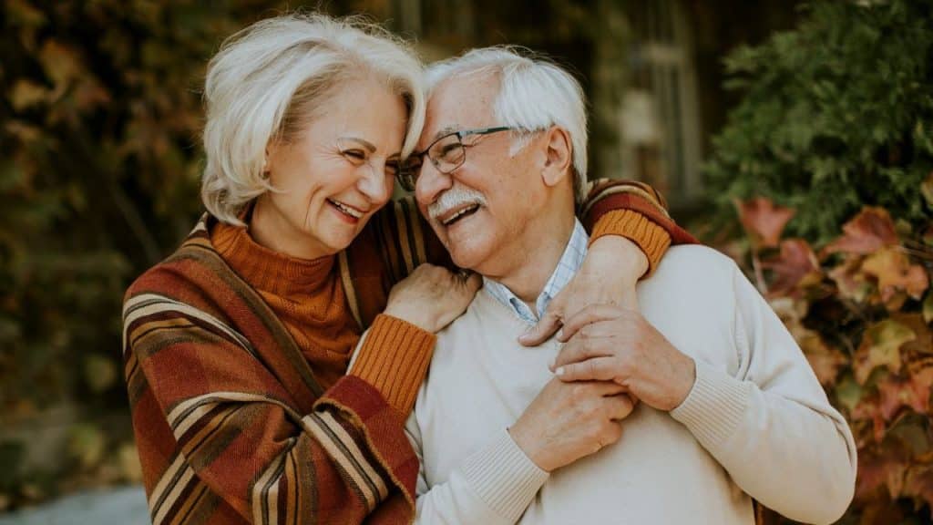 A joyful elderly couple embraces outdoors, surrounded by autumn foliage.