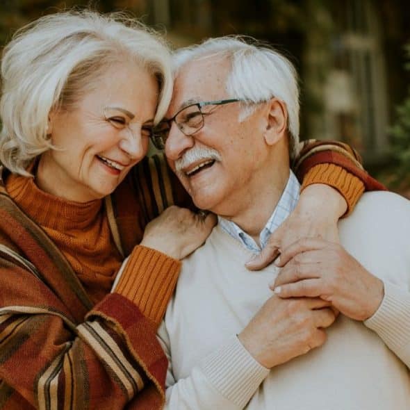 A joyful elderly couple embraces outdoors, surrounded by autumn foliage.