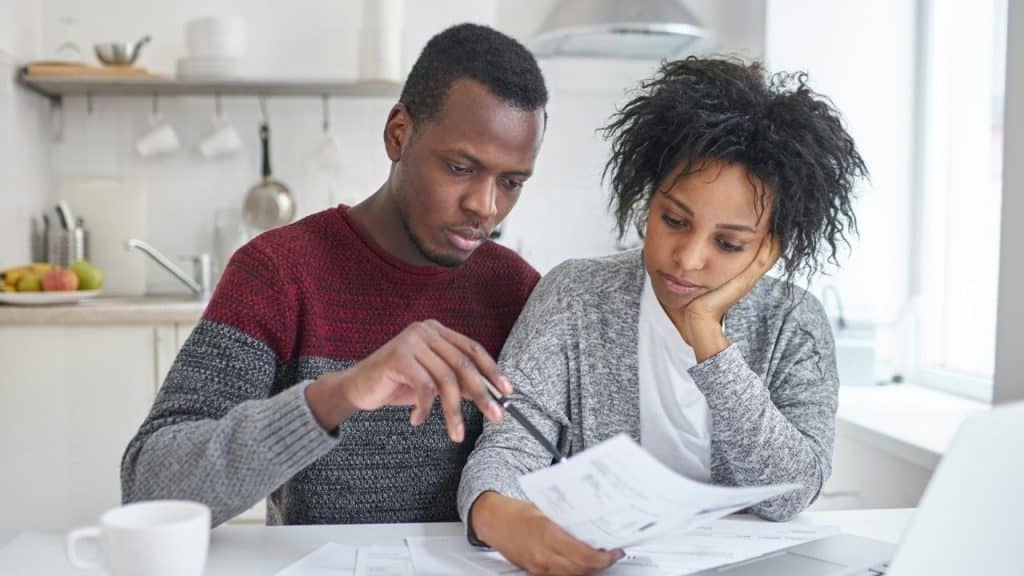 A focused man and a woman looking stressed review documents together in a kitchen.