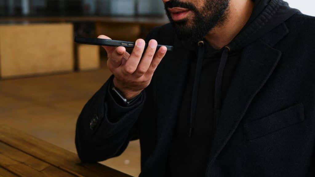 A person speaking into a smartphone while sitting at a table.