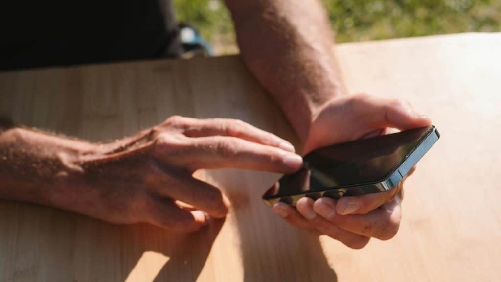 A person using a smartphone outdoors at a wooden table.
