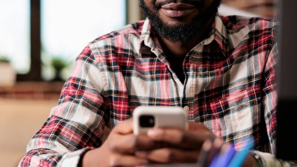 A person sitting indoors wearing a plaid shirt and holding a smartphone.