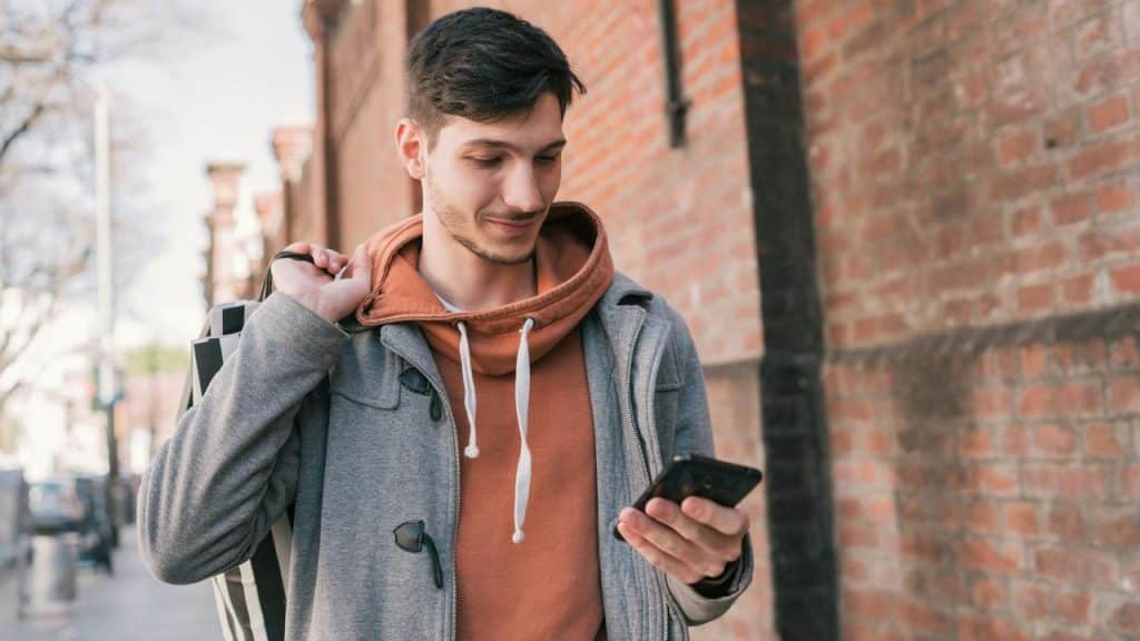 A person walking outside by a brick wall while looking at their phone.