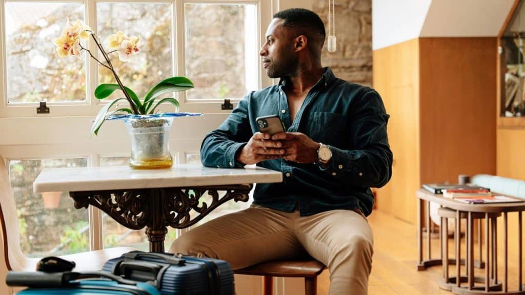 A person sitting indoors by a window holding a smartphone and looking outside.