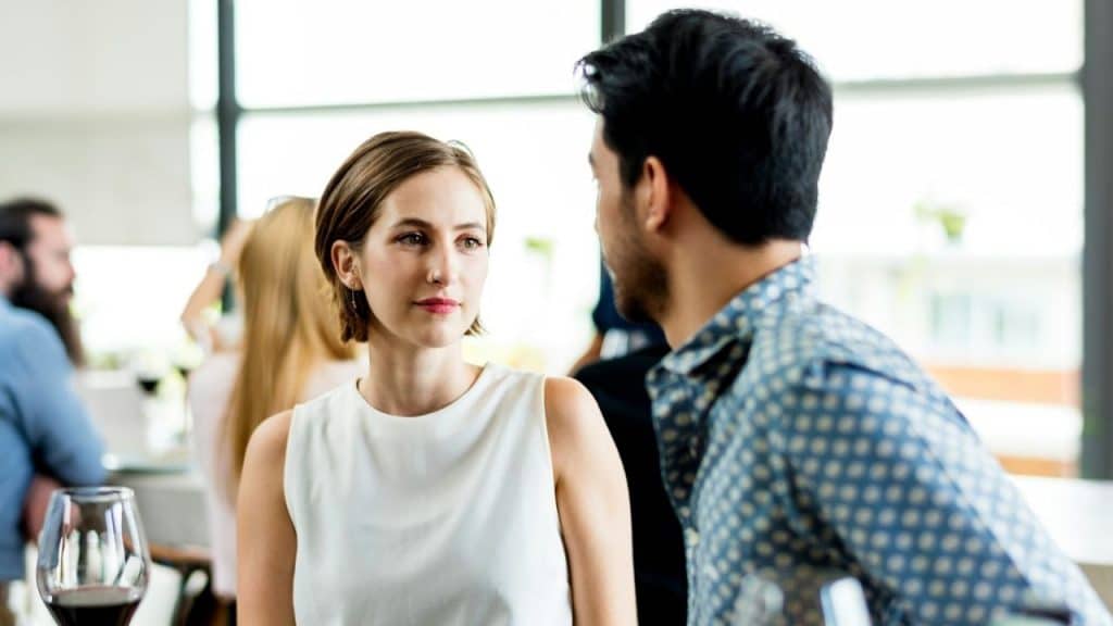 Woman in a white top looking at a man in a patterned shirt in a crowded room.
