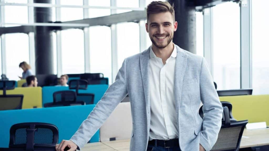 Smiling man in a light blazer and white shirt in a modern office setting.