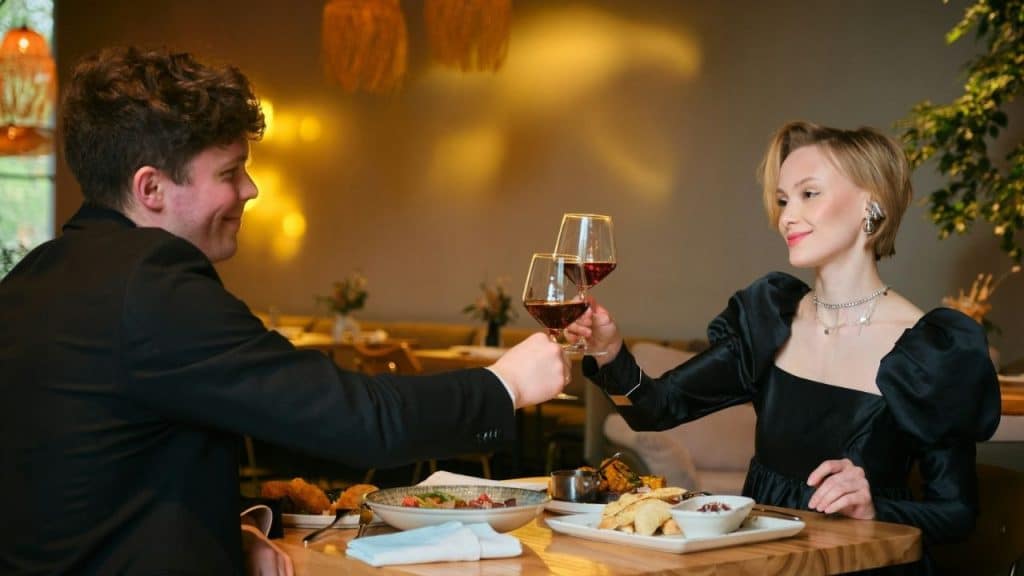 Couple on a date toasting with red wine glasses over a meal in a restaurant.
