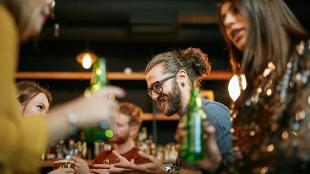 Group of young adults socializing in a bar, holding bottles and glasses.