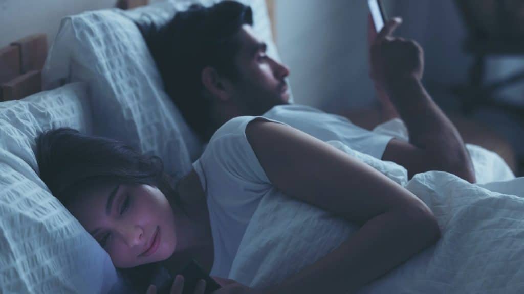 A couple using mobile phones in their bed.