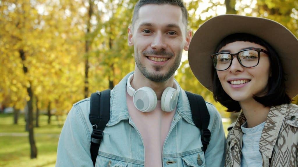 A smiling couple poses outdoors in autumn.