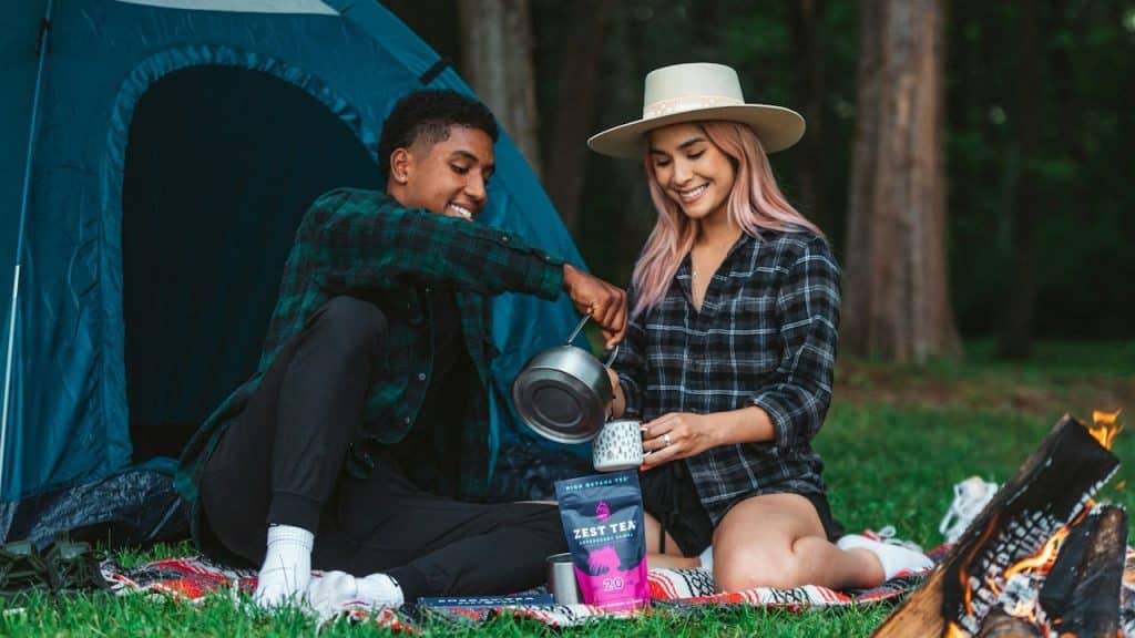 A man and woman sitting on a blanket next to a tent.
