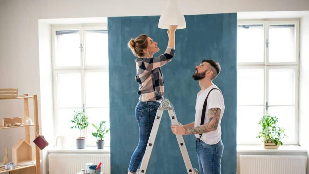 A couple changing a lightbulb indoors at home relocation.