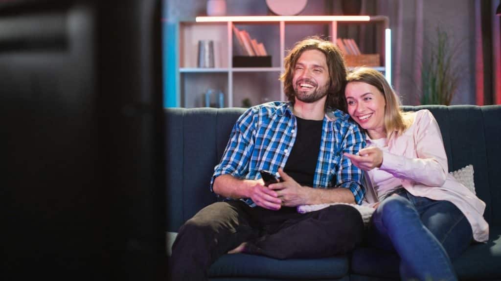 A young man and woman smiling sincerely while watching comedy on TV.