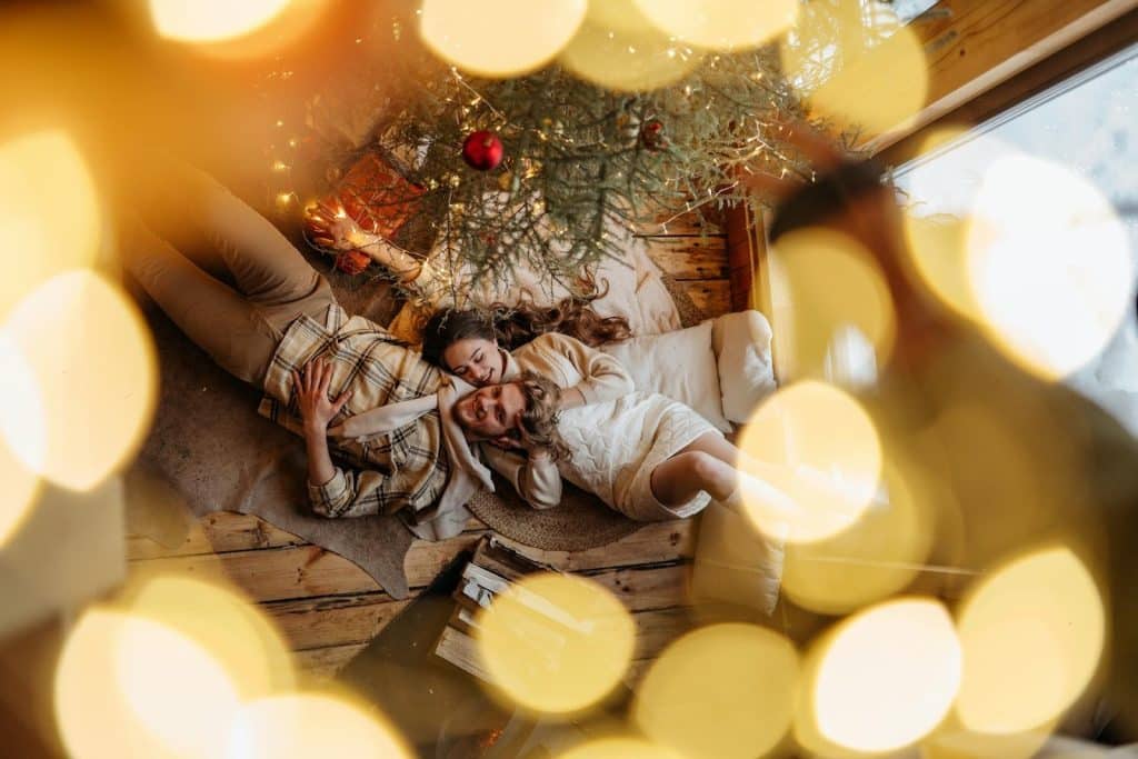 The couple is lying under the Christmas tree.