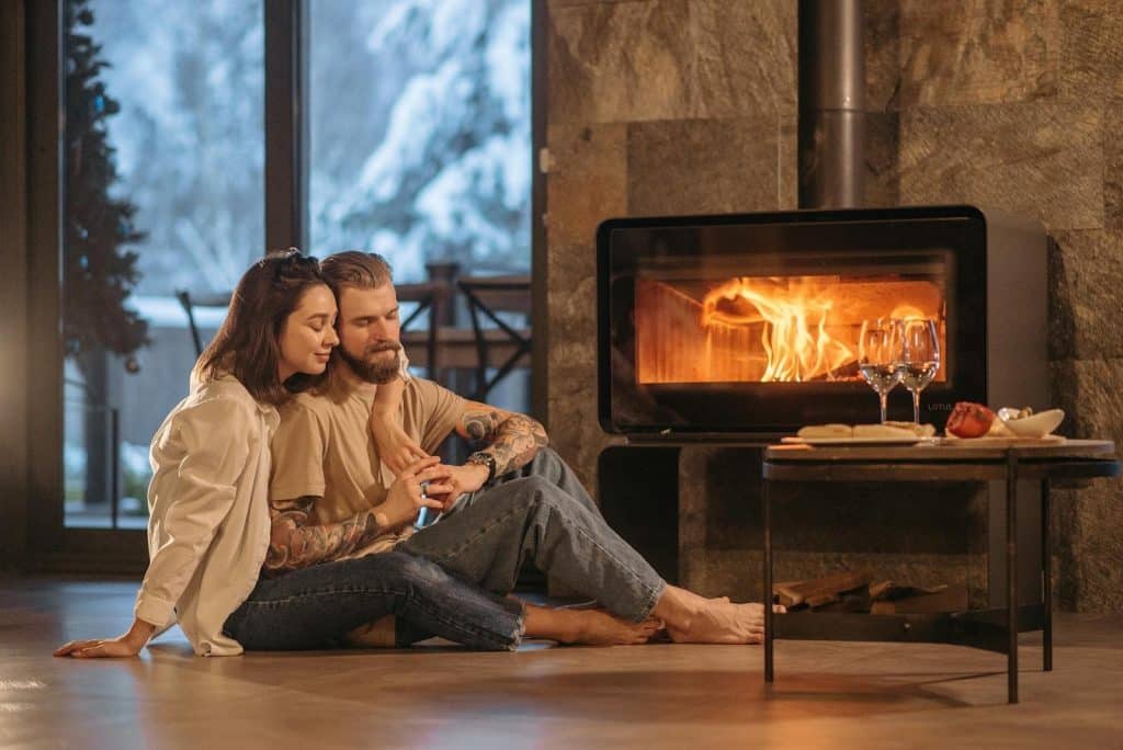 The man and the woman are sitting on the floor near the fireplace.