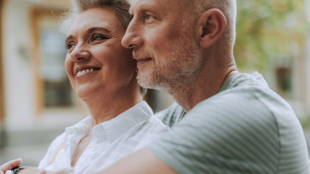 Close-up of a smiling older couple embracing and looking into the distance outdoors.