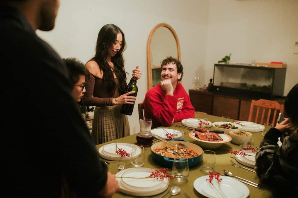 The man is looking at the woman opening a bottle of wine.