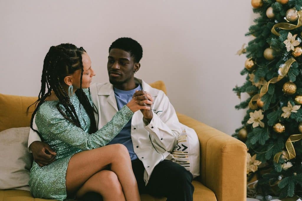 The couple is sitting on a sofa next to a Christmas tree.