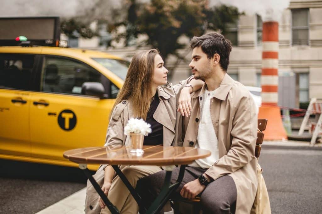 The couple is sitting at a table beside the street.