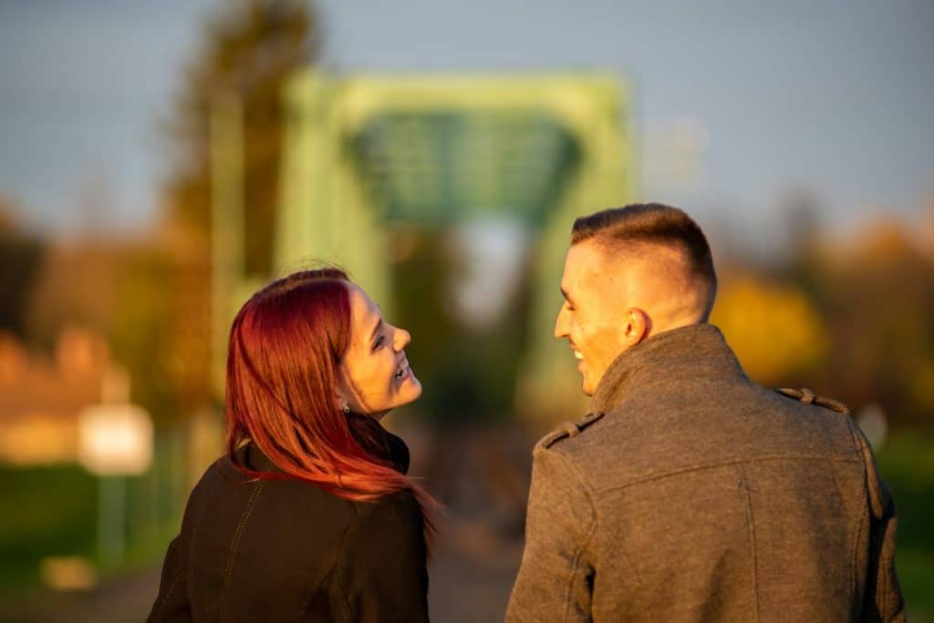 The woman and the man are smiling at each other while walking outside in the daytime.