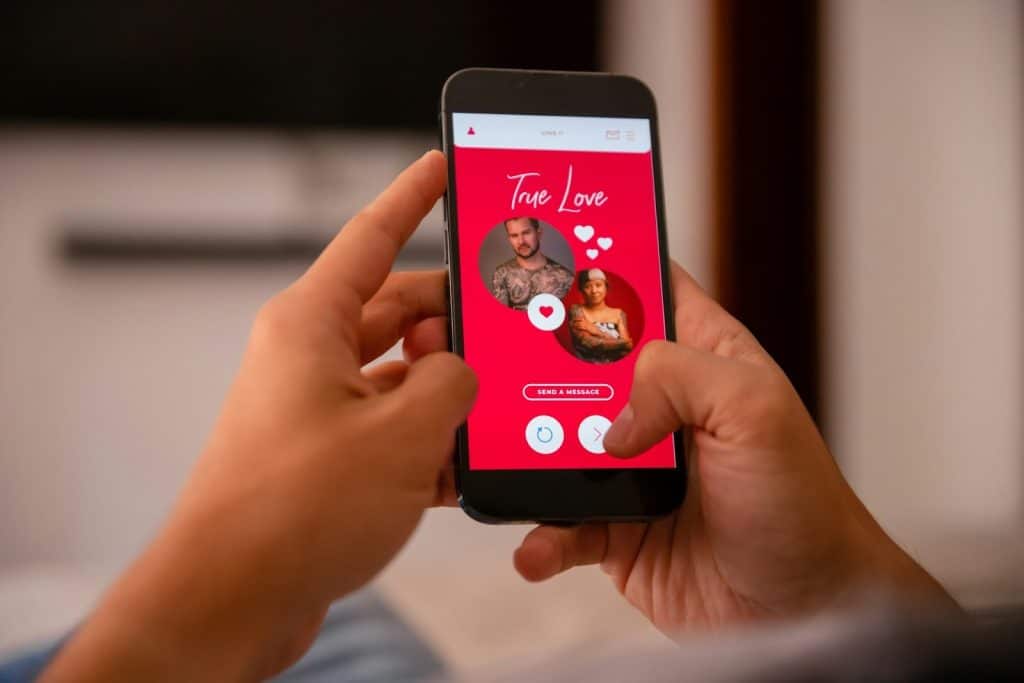 The person is holding a cellphone with a dating app displayed on the screen.