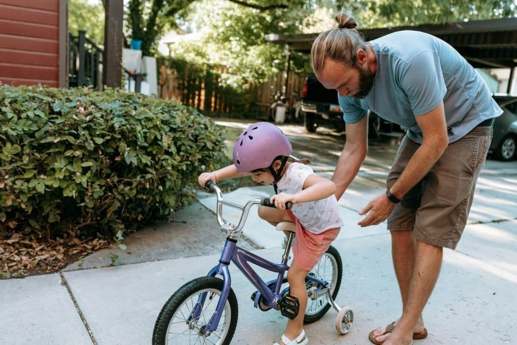 The man is teaching his daughter how to ride a bike.