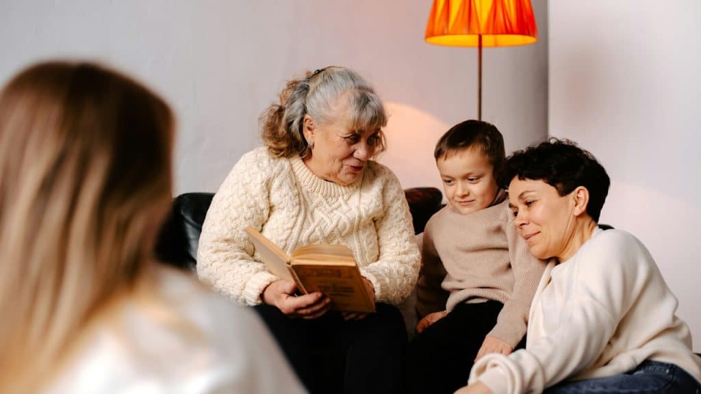 An elderly woman sitting on a couch reading a book to her grandson.