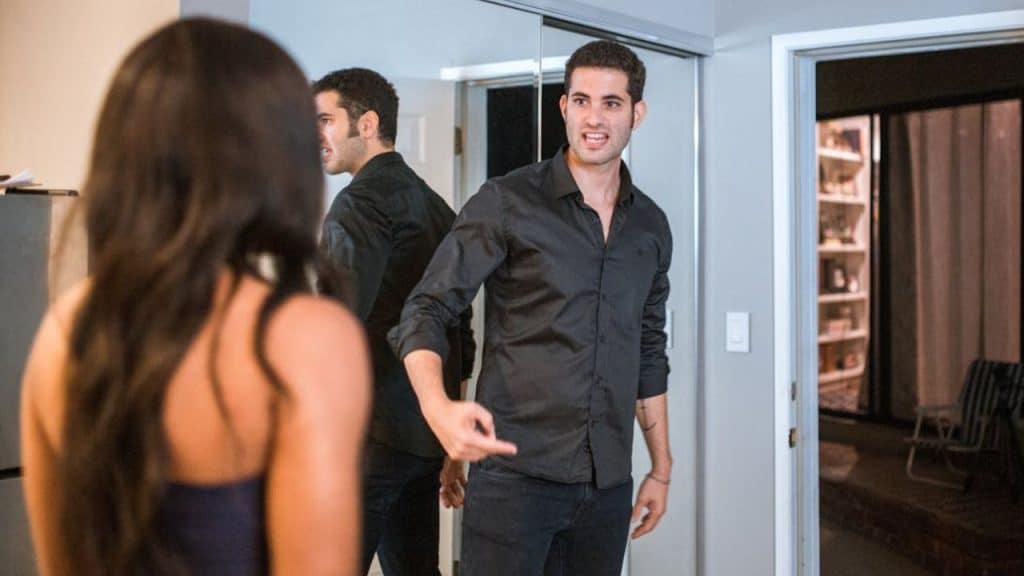 A man in a black shirt is speaking firmly, pointing at a woman whose back is to the camera.