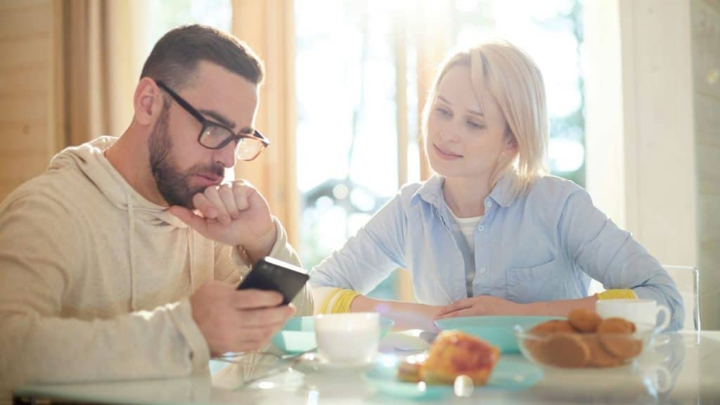 Man absorbed in his phone while a woman looks at him during breakfast.
