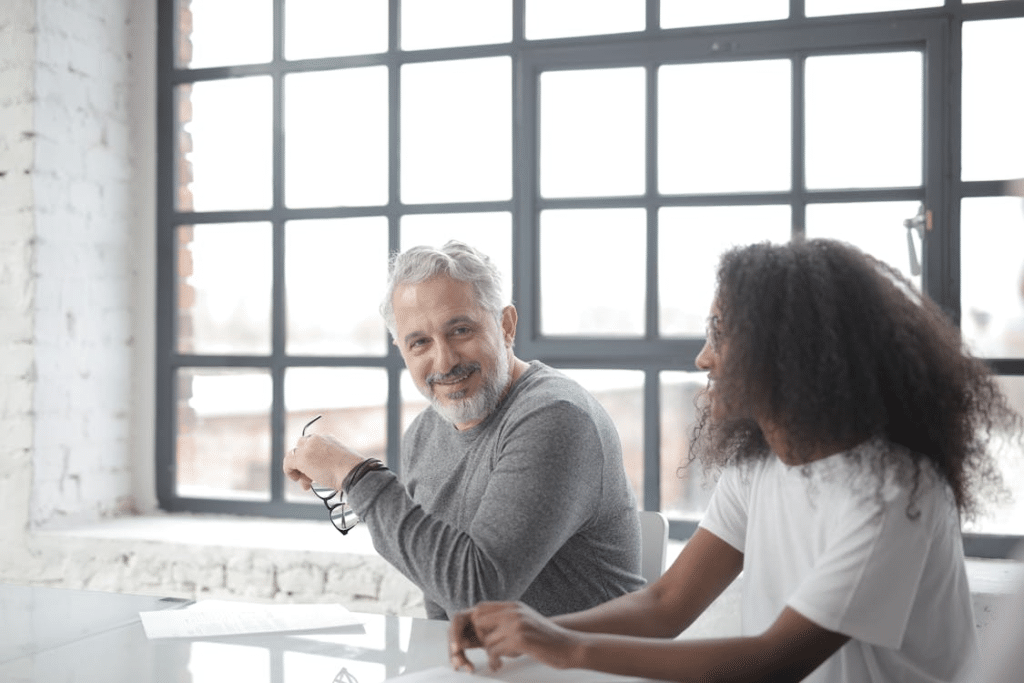 Cheerful senior gray haired man supporting young woman in office