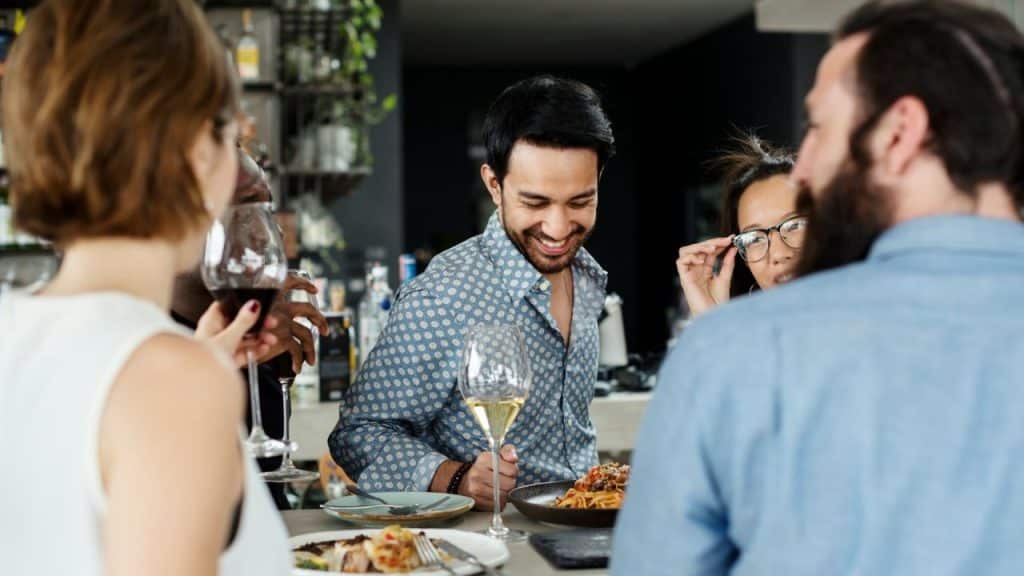 Group of diverse friends socializing and drinking wine around a table in a bar or restaurant.