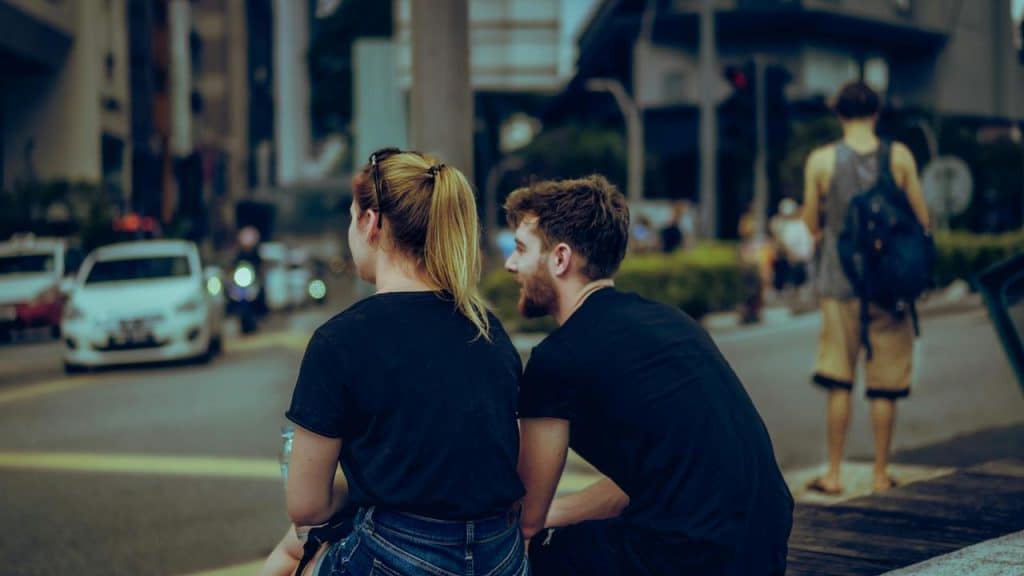 A man and woman seated along a city street sharing a conversation.