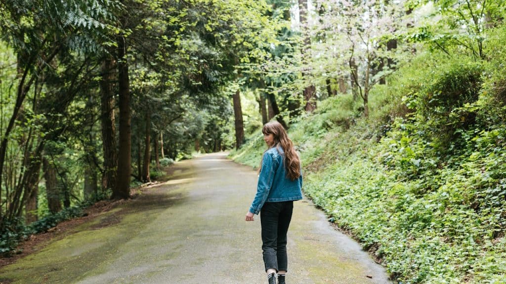 A woman walking down a road in the woods.