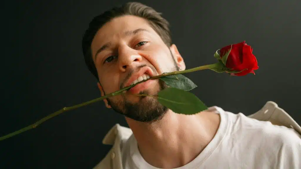 A middle-aged man holding a red rose in his mouth.